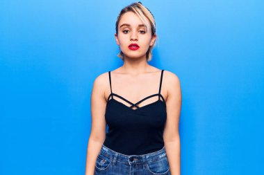 Yüzünde ciddi bir ifade olan sıradan kıyafetler giyen genç, güzel sarışın bir kadın. Basit ve doğal bir şekilde kameraya bakıyorsun.. 