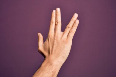 Kafkasyalı genç adam parmaklarını izole edilmiş mor arka planda gösteriyor Vulkan selamı veriyor, el ve parmaklarının arkasını gösteriyor, ucube kültürü sergiliyor.