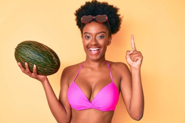 Genç Afro-Amerikalı kadın elinde kavun, elinde bir fikirle gülümsüyor ya da soru işareti yapıyor. 