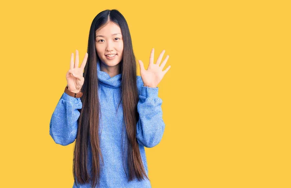 若いです美しいです中国人女性身に着けていますカジュアルTurtleeckセーターショーと指差し指番号8ながら笑顔自信と幸せ — ストック写真