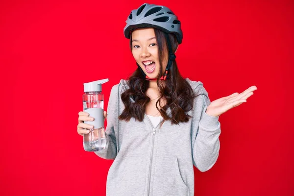 若い美しい中国の女の子は自転車のヘルメットを着て 幸せな笑顔で達成を祝う水ボトルを保持し 手を上げと勝者の式 — ストック写真