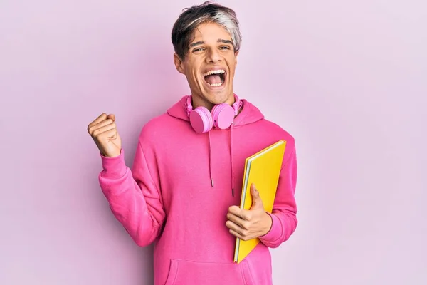 Jovem Hispânico Homem Segurando Livro Usando Fones Ouvido Gritando Orgulhoso — Fotografia de Stock