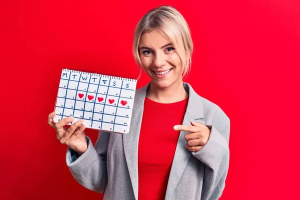Piękna Blondynka Kontroli Miesiączki Gospodarstwa Okres Kalendarz Czerwonym Tle Uśmiechając — Zdjęcie stockowe