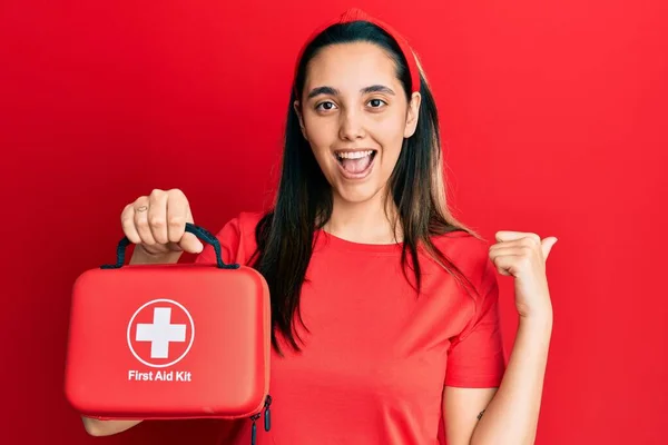 Young Hispanic Woman Holding First Aid Kit Pointing Thumb Side — Stock Photo, Image