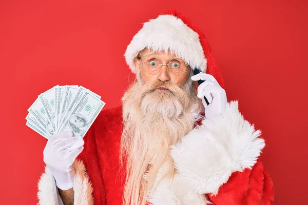 Staruszek Kostiumie Świętego Mikołaja Trzymający Dolary Nadęty Smartfon Śmieszną Twarzą — Zdjęcie stockowe