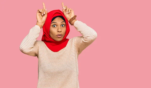 身穿传统伊斯兰头巾的年轻非洲裔美国女人做着滑稽的手势 头戴头戴牛角 — 图库照片