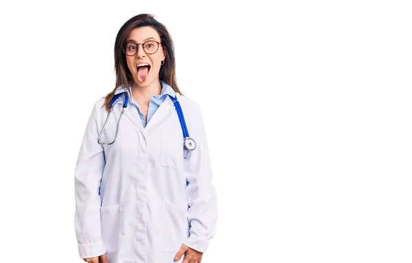 年轻漂亮的女人带着医生听诊器和眼镜 带着滑稽的表情 伸出舌头 高兴极了 情感概念 — 图库照片