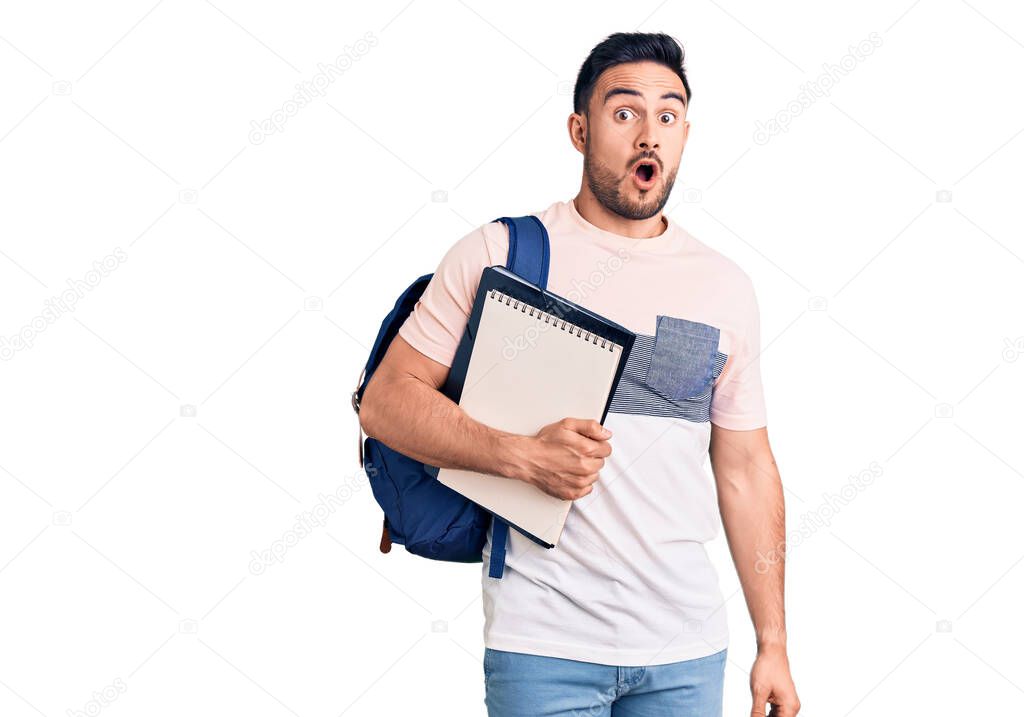 Young handsome man wearing student backpack and notebook scared and amazed with open mouth for surprise, disbelief face 
