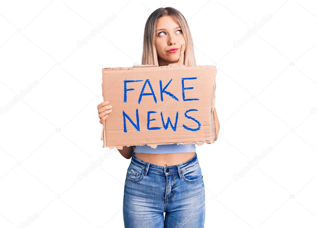 Young beautiful blonde woman holding fake news banner serious face thinking about question with hand on chin, thoughtful about confusing idea 