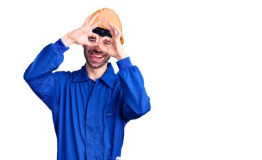 İşçi üniforması giyen genç bir İspanyol dürbün gibi jest yapıyor, gözleri parmaklarından bakıyor. çılgın ifade. 