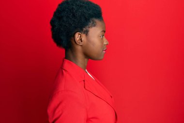 Afro-Amerikalı genç bir kız iş kıyafetleri giyiyor. Taraf arıyor, rahat poz veriyor. Kendine güvenen bir gülümsemeyle doğal bir yüz ifadesi takınıyor.. 