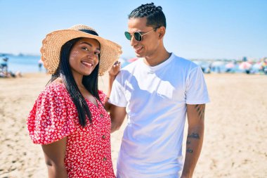 Genç Latin çift, mutlu bir şekilde gülümsüyor ve sahilde sarılıyorlar..