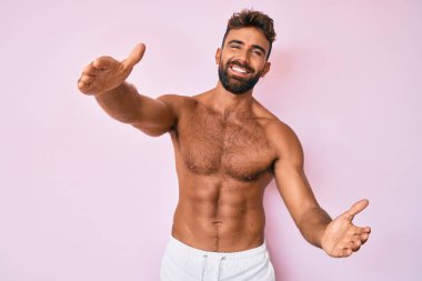 Latin asıllı genç adam kameraya kollarını açıp sarılmak için gülümsüyor. Mutluluğu kucaklayan neşeli bir ifade.. 