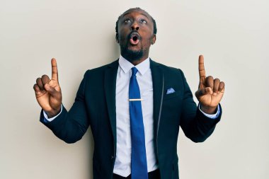 Yakışıklı, takım elbiseli ve kravatlı genç bir adam şaşırmış ve şaşırmış bir şekilde yukarı bakıyor ve parmaklarıyla işaret ediyor ve kollarını kaldırıyordu.. 