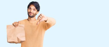 Yakışıklı ispanyol adam elinde kızgın suratlı paket kağıdı tutuyor, olumsuz işaret baş parmakları aşağıda, reddedilme konsepti. 