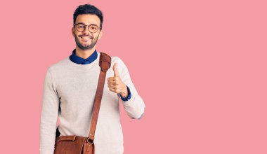 Deri çanta giyen, mutlu ve pozitif gülümseyen genç, yakışıklı İspanyol adam, mükemmel ve onay işareti yapıyor. 