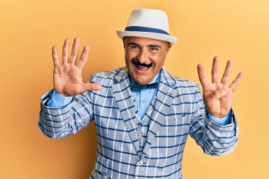 Olgun, orta doğulu bıyıklı, klasik ve şık moda tarzlı bir adam dokuz numarayı gösterip gösterirken kendine güvenen ve mutlu bir şekilde gülümsüyor.. 