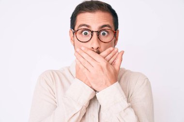 Gündelik kıyafet ve gözlük takan genç yakışıklı adam yanlışlıkla elleri ile ağzını kapatırken şok oldu. gizli kavram. 