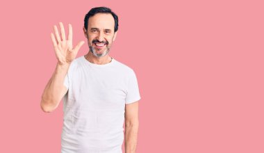 Orta yaşlı yakışıklı bir adam gündelik tişört giyer ve parmaklarıyla beş numarayı gösterirken kendinden emin ve mutlu gülümserdi.. 