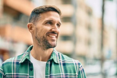 Genç beyaz adam gülümseyerek şehirde mutlu mesut duruyor..