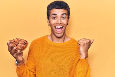 Genç Afrikalı Amerikalı adam elinde bademlerle başparmağını kaldırmış, ağzı açık gülümsüyor. 
