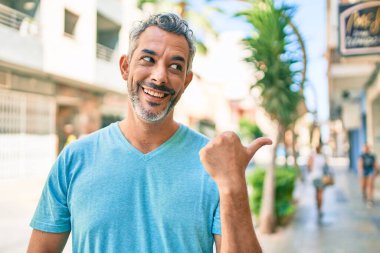Şehrin caddesinde günlük kıyafetler giyen, gülen yüzlü gülümseyen ve baş parmağıyla yüzünü gösteren orta yaşlı, gri saçlı bir adam.. 