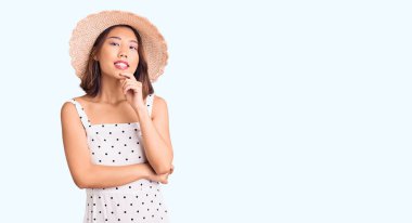 Yaz şapkası takan genç güzel Çinli kız kameraya kendinden emin bakıyor kollarını kavuşturmuş ve çenesini kaldırmış gülümsüyor. Olumlu düşünmek. 