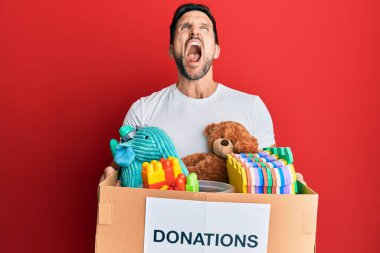 Genç ve yakışıklı bir adam oyuncaklarla dolu bir bağış kutusu tutuyor kızgın ve kızgın çığlıklar atıyor öfkeyle bağırıyor, öfkeyle yukarı bakıyor.. 
