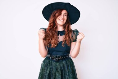 Cadı cadılar bayramı kostümü giyen genç ve güzel bir kadın çok mutlu ve heyecanlı. Kazanan jestler yapıyor. Kolları havada, gülümsüyor ve başarı için bağırıyor. kutlama konsepti. 