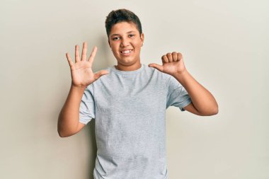 Gündelik gri tişört giyen genç İspanyol çocuk altı numarayı gösterip işaret ederken kendinden emin ve mutlu gülümsüyor.. 