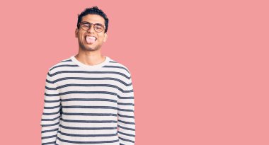 Gündelik kıyafetler giyen ve gözlük takan İspanyol yakışıklı genç adam komik bir ifadeyle dilini dışarı çıkartıyor. duygu kavramı. 