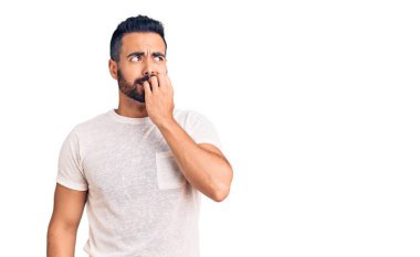 Günlük kıyafetler giyen genç İspanyol adam gergin ve gergin görünüyor. Ağzı tırnak yiyen eller. anksiyete. 