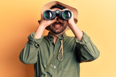 Kaşif şapkası takan genç İspanyol adam elinde dürbün tutarken pozitif ve mutlu görünüyor. Kendine güvenen bir gülümsemeyle dişlerini gösteriyor. 