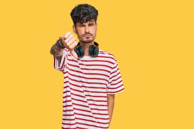Genç İspanyol adam kulaklık takarak müzik dinliyor mutsuz görünüyor ve reddediliyor ve olumsuz jestler yapıyor. kötü ifade. 