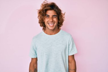 Gündelik kıyafetler giyen genç İspanyol adam kameraya seksi bir ifadeyle bakıyor, neşeli ve mutlu bir yüzle.. 