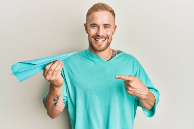 Elinde kağıt uçak tutan genç beyaz adam mutlu bir şekilde elini ve parmağını gösterdi. 