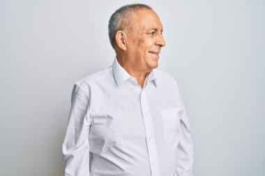 Yakışıklı, beyaz tişört giyen, yüzünde gülümseme ve doğal ifadeyle yan yana bakan biri. Kendinden emin gülen. 