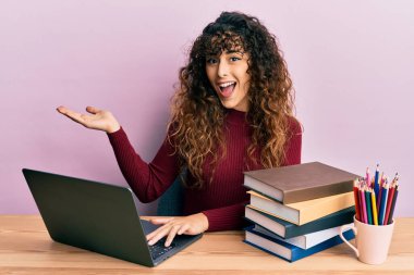 Genç İspanyol kız dizüstü bilgisayar ve kitapları kullanarak başarıyı mutlu bir gülümsemeyle ve kazanan yüz ifadesiyle kutluyor. 