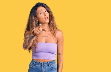 Dövmeli genç İspanyol bir kadın. Sıradan kıyafetler giyiyor. Kameraya kızgın ve sinirli bir şekilde bakıyor. 