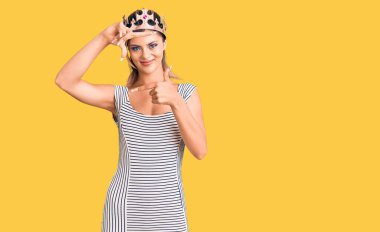 Kral tacı takan genç ve güzel bir kadın gülümsüyor ve mutlu yüzlü eller ve parmaklarla çerçeve yapıyor. yaratıcılık ve fotoğrafçılık kavramı. 