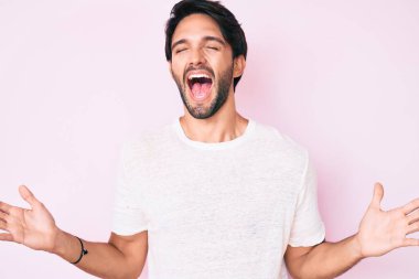 Yakışıklı, beyaz tişörtlü, çılgın ve çılgın başarısını kutlayan kolları havada ve gözleri kapalı heyecanlı bir adam. Kazanan konsept 