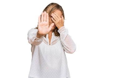 Orta yaşlı, beyaz gömlek giyen, gözlük takan, ellerle gözleri kapayan, üzgün ve korku ifadeli orta yaşlı sarışın bir kadın. utangaç ve olumsuz kavram. 