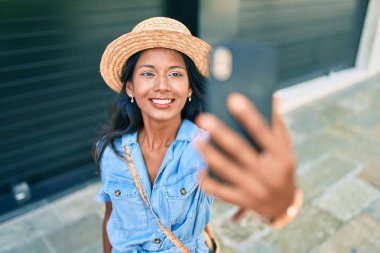 Genç, güzel Hintli bir kadın, yaz şapkası takıyor, gülümsüyor, mutlu bir şekilde şehrin akıllı telefonunda selfie çekiyor..