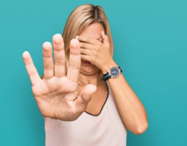 Orta yaşlı beyaz kadın gündelik giysiler giyip elleriyle gözlerini kapatıyor ve üzgün ve korku ifadeleriyle dur hareketi yapıyor. utangaç ve olumsuz kavram. 