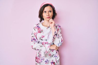 Gündelik kıyafetler giyen genç ve güzel bir kadın. Ciddi bir yüz ifadesi. Elleri çenesinde soru soran, kafa karıştırıcı fikirleri düşünen. 