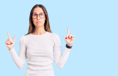 Güzel esmer, beyaz süveter giyen, gözlüklü, üzgün ve üzgün görünen, yönünü parmaklarıyla gösteren mutsuz ve depresif genç bir kadın.. 