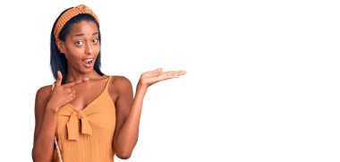 Genç Afrikalı Amerikalı kadın yazın giydiği kıyafetle kameraya hayret ediyor ve gülümsüyor.. 