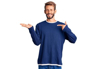 Sarışın, sakallı, sıradan bir süveter giyen yakışıklı adam kameraya hayret ediyor ve gülümsüyor.. 