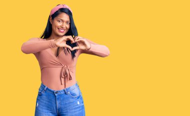 Uzun saçlı, gündelik kıyafetler giyen, aşık gülümseyen, kalp sembolü ve elleri olan İspanyol bir kadın. romantik kavram. 