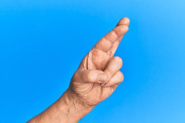 Mavi izole edilmiş arka plan üzerinde yaşlı İspanyol adamın eli. Parmakları çapraz, batıl inançlar ve şanslı bir jest, şanslı ve umut ifadesi. 